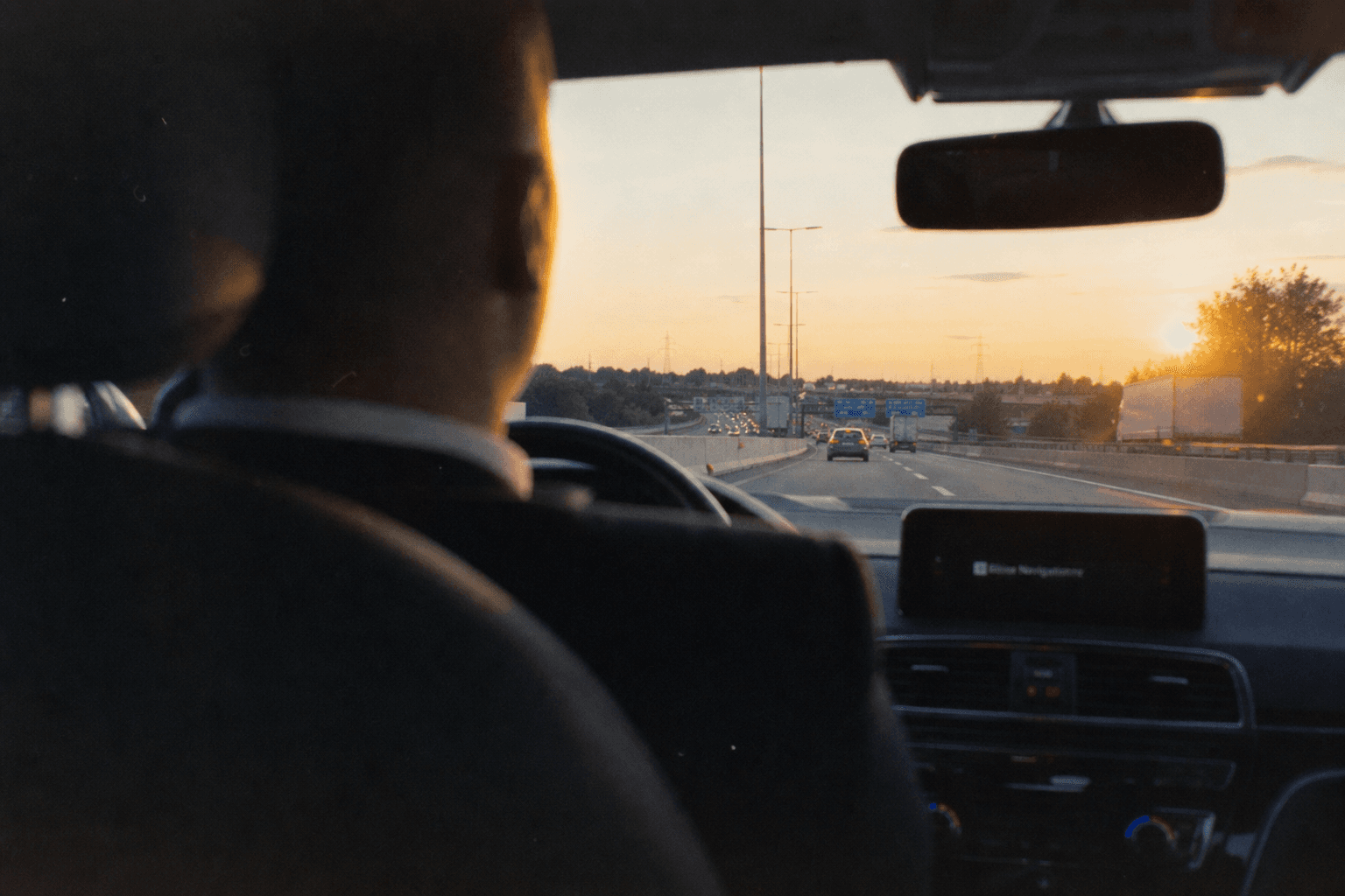 Zicht vanaf de achterbank naar de snelweg bij zonsondergang, hoofdsteun van de chauffeur op de voorgrond