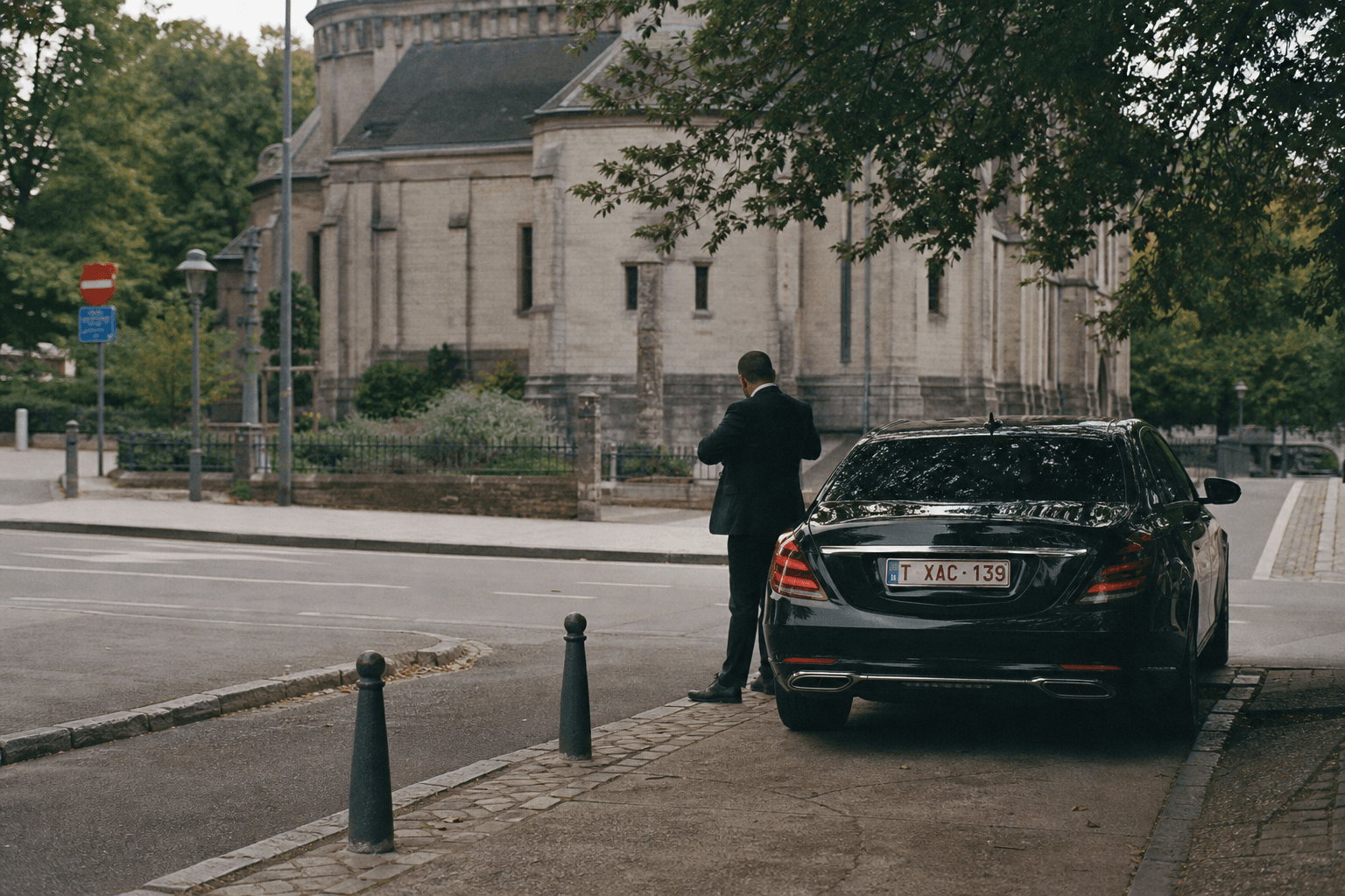 Chauffeur de dos ajustant sa veste près de son véhicule premium garé