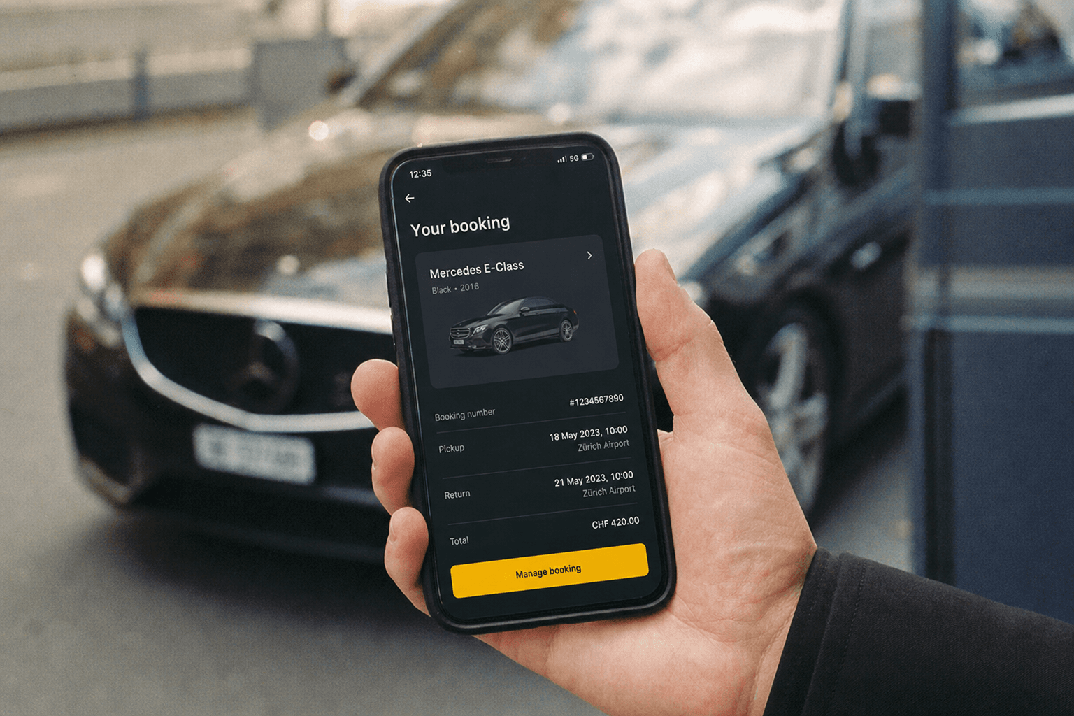 Main tenant un smartphone avec un écran de réservation, véhicule premium flou à l'arrière-plan